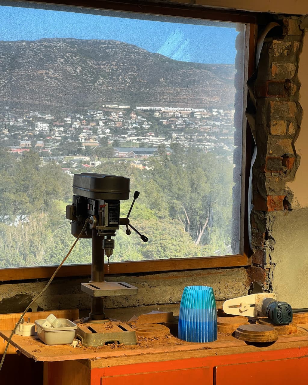 A workshop showing a drill press with a hillside in the background./