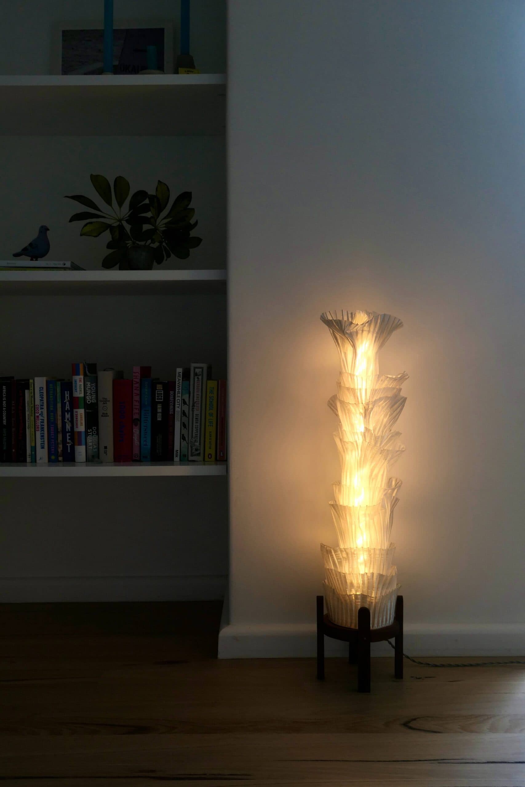 Heel Turn Floor Lamp switched on beside a bookshelf, a tall column of stacked flares lighting the wall